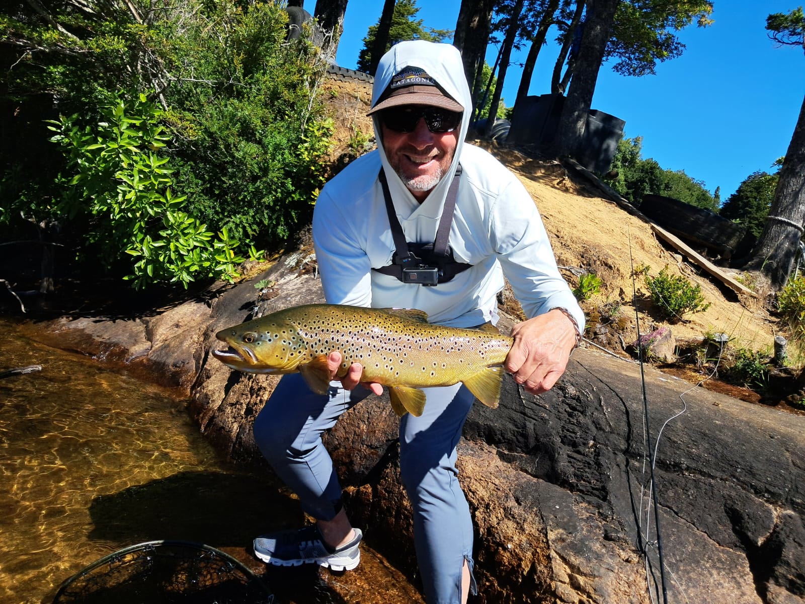 Angler with a golden brown trout on sunlit rocks in Chile